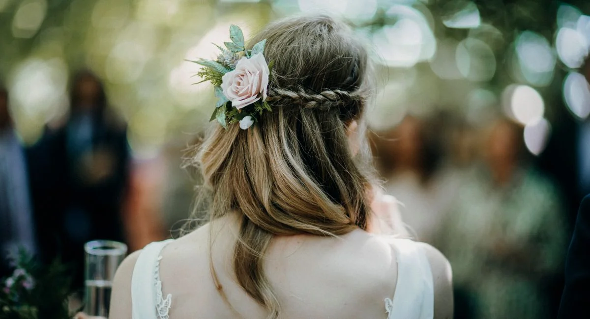 Elegant back view of a woman with braided hair and a floral accessory, outdoors.