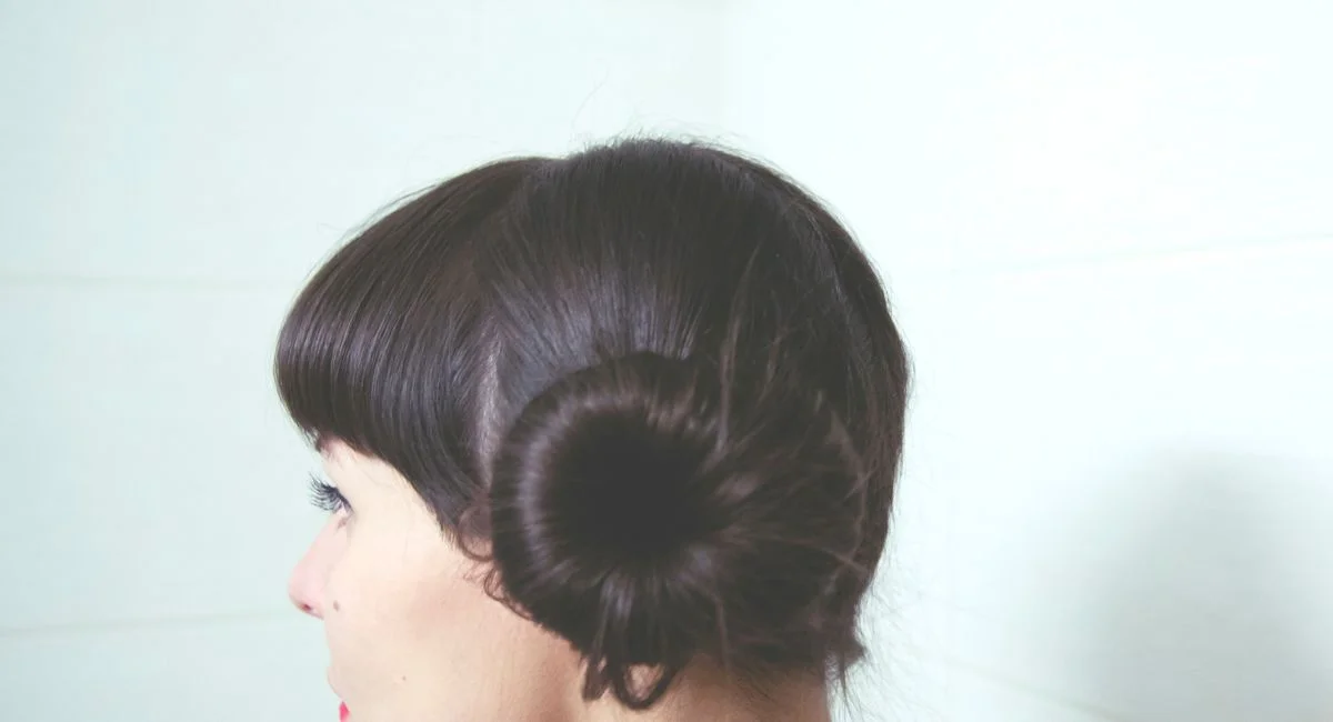 Side view of dark haired female with bun on head standing against white tiled wall