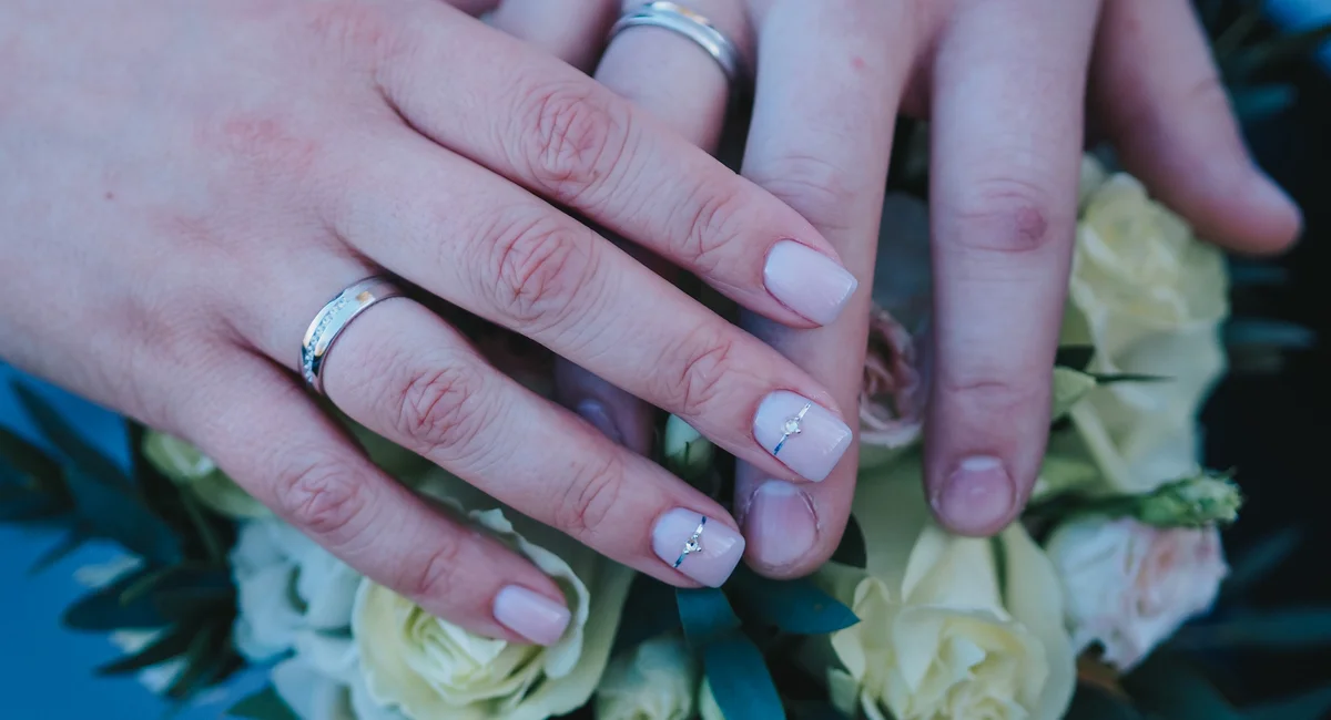 Close-up of couple's hands with wedding rings resting on a bridal bouquet.
