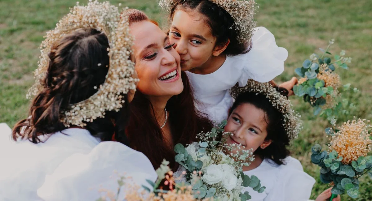 A happy mother with her daughters wearing white dresses and flower crowns.