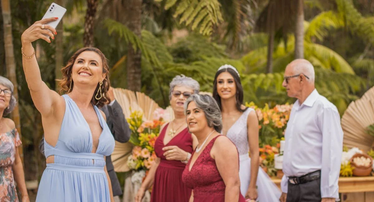 Guests and bride enjoying an outdoor wedding reception while capturing a group selfie for memories.