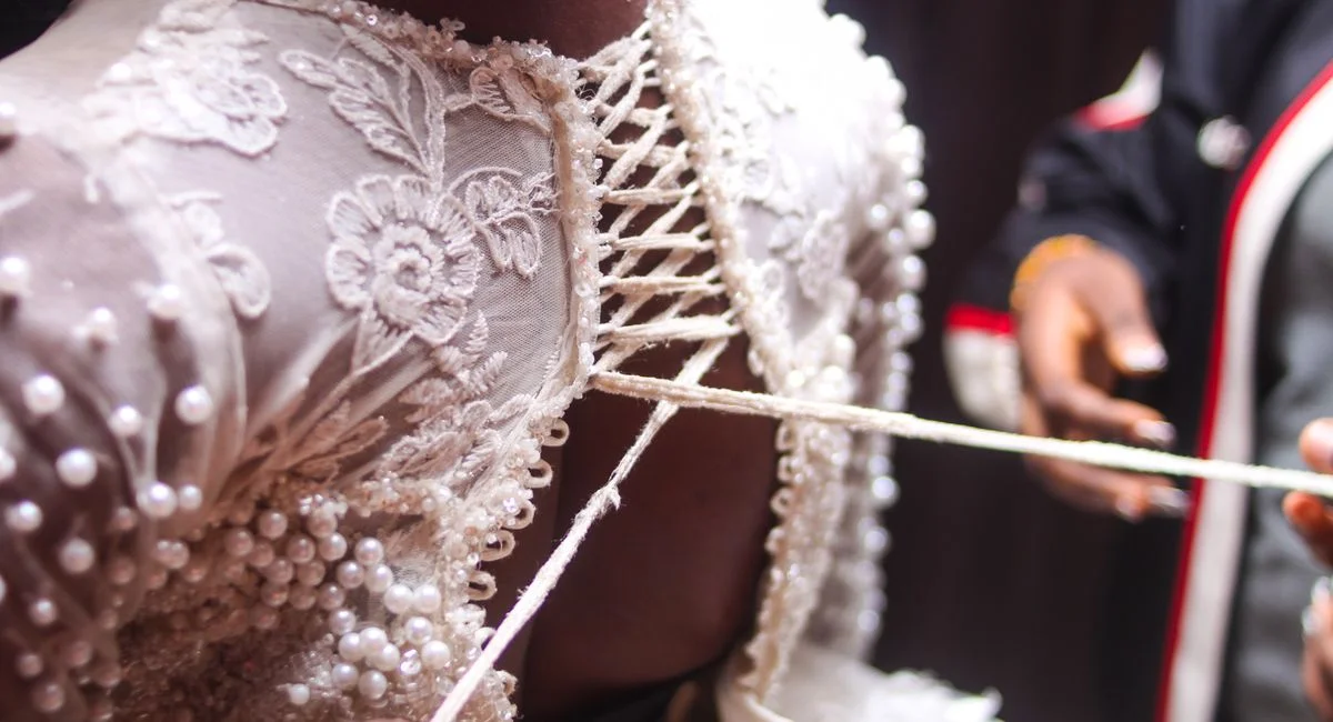 Detailed close-up of a bride's lace-up bridal gown being fitted, showcasing delicate lace embroidery.