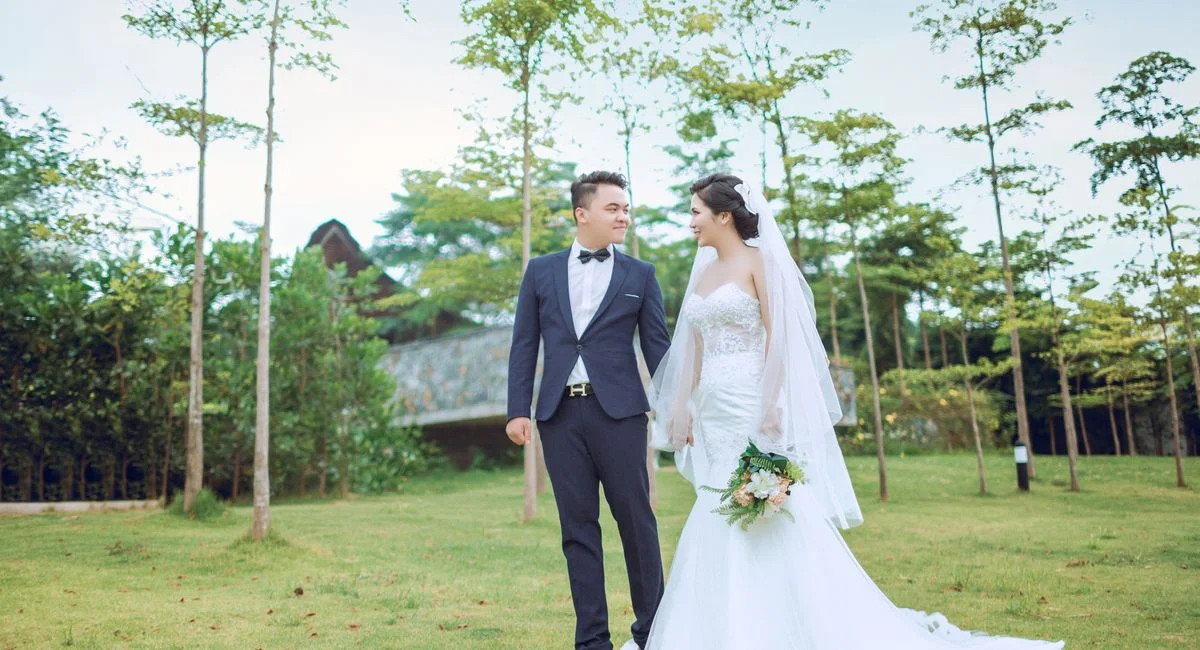 A romantic couple enjoying their wedding day, elegantly dressed, in a beautiful park setting.